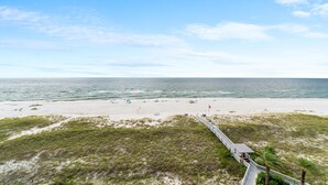 A beach with a boardwalk leading to a building, a sandy beach, and the ocean. - Spanish Key 603 (Pensacola)