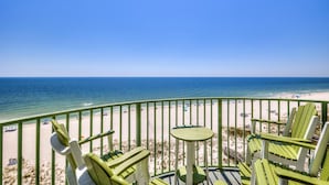 A balcony with green Adirondack chairs and a small round table overlooking a beach with a clear blue sky. - Perdido Towers West 907 (Pensacola)