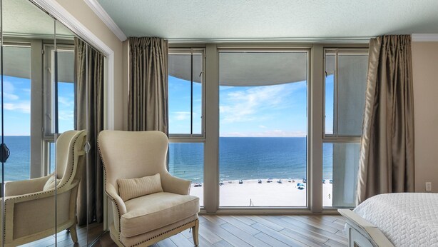 A hotel room with a large window, a bed, a chair, and a view of the beach. - Perdido Towers West 907 (Pensacola)
