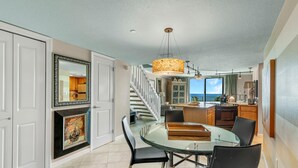 A modern kitchen with a dining area, featuring a glass table, black chairs, and a large pendant light. - Perdido Towers West 907 (Pensacola)