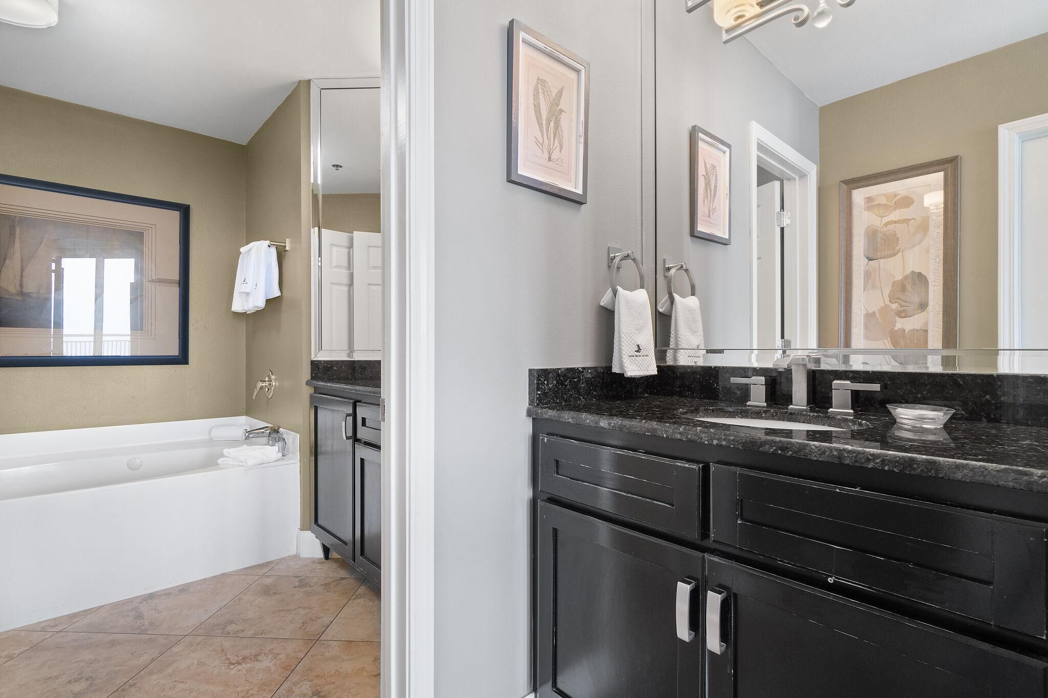 A modern bathroom with a bathtub, dark cabinetry, and artwork on the walls.