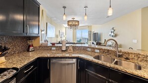 A modern kitchen with granite countertops, stainless steel appliances, and a central island. - Palacio 1803 (Pensacola)