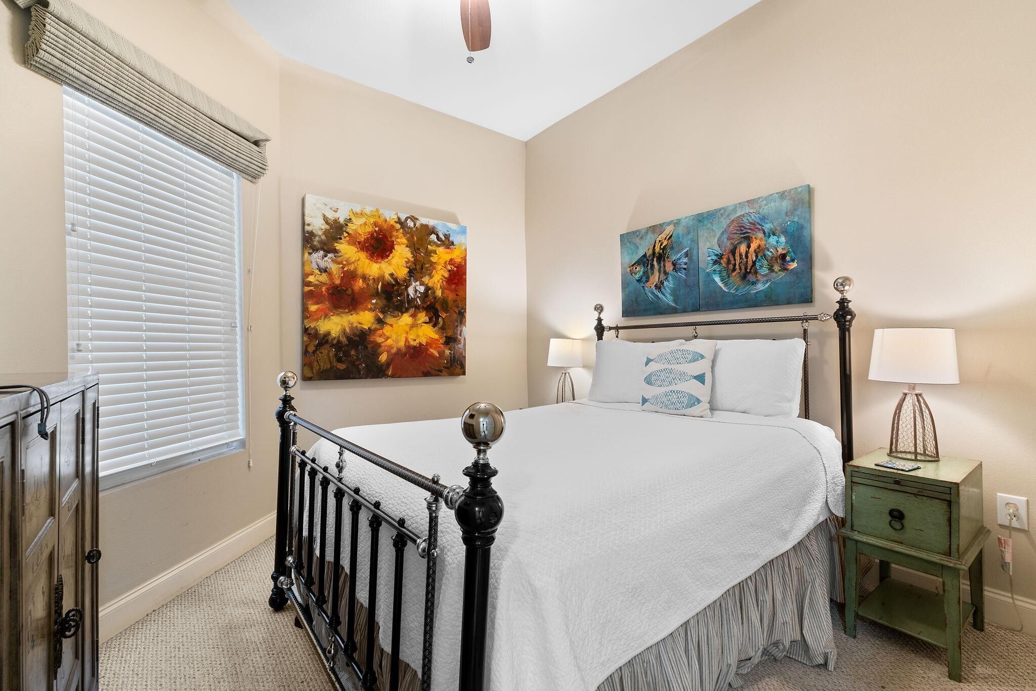 A bedroom with a bed, a nightstand, a lamp, and two paintings on the wall.