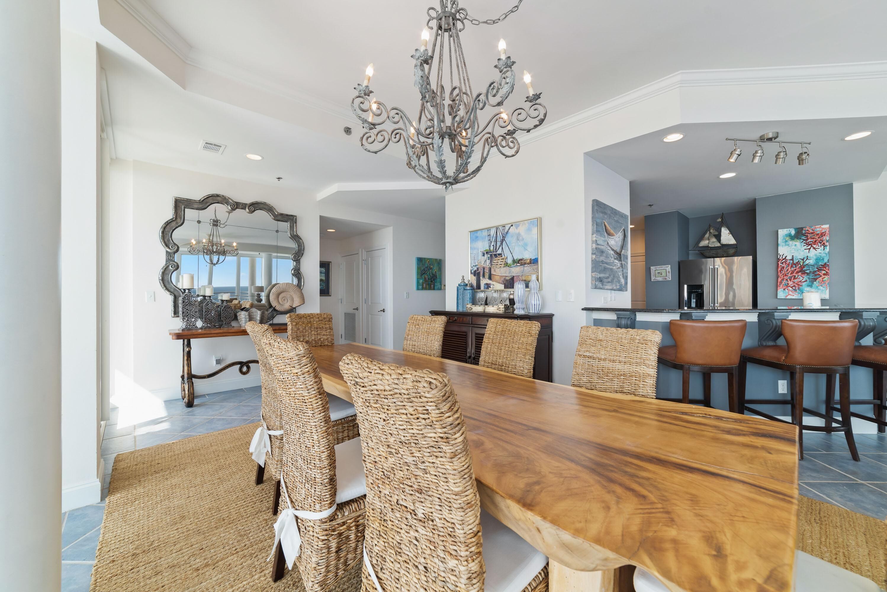 A spacious dining area with a long wooden table, wicker chairs, and a chandelier.