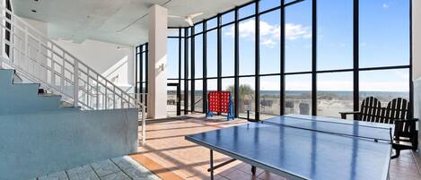 Une table de ping-pong se trouve dans une pièce spacieuse, dotée de grandes fenêtres et d’un escalier.