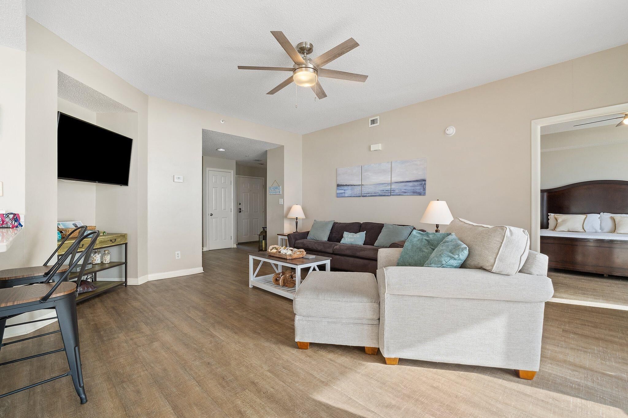 A modern living room with a ceiling fan, a flat-screen TV, a sofa, a coffee table, and a dining area with chairs.