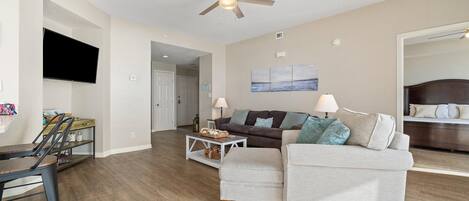 A modern living room with a ceiling fan, a flat-screen TV, a sofa, a coffee table, and a dining area with chairs.
