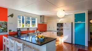 Una cocina moderna con una isla central, muebles de color blanco y naranja, un ventanal y vistas al exterior.