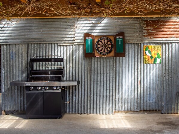 Una zona de cocina con estufa a gas, microondas y un dardo fijado a una pared de metal corrugado.