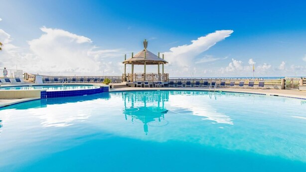 A clear blue pool with lounge chairs, a gazebo, and a view of the ocean. - Summer House 203a (Orange Beach)