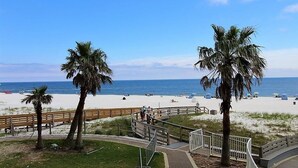 A beach with palm trees, a wooden walkway, and a sandy beach area. - Summer House 203a (Orange Beach)
