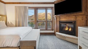 Camera d'albergo con un grande letto, un caminetto, una TV a parete e vista sulle montagne dalle finestre.