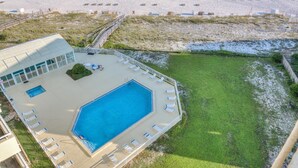 A pool area with a view of the beach, a grassy lawn, and a building with a glass facade. - Perdido Sun 916 (Pensacola)