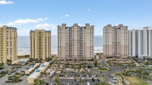A coastal high-rise hotel with multiple floors, a parking area, and a view of the ocean. - Indigo East 2001 (Pensacola)
