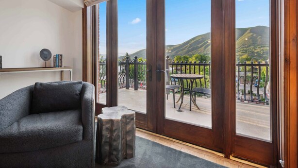 A room with a large window overlooking a balcony with a view of hills and a street.
