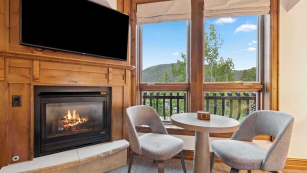 A cozy room with a fireplace, a television mounted above it, and a balcony with a view of the outdoors.