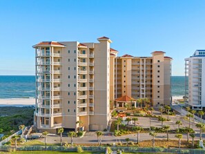 A multi-story hotel with balconies, a beach view, and a parking area with palm trees. - Vista Del Mar 303 (Pensacola)