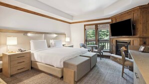 Une chambre d’hôtel moderne dotée d’un grand lit, d’une télévision à écran plat, d’une cheminée et d’un balcon offrant une vue sur les arbres.