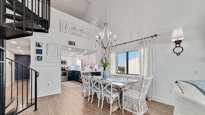A spacious dining area with a chandelier, white wicker chairs, and a view to the kitchen. - Shipwatch C301 (Pensacola)
