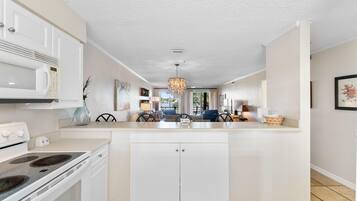 A modern kitchen with white cabinetry, a built-in stove, and a dining area with a chandelier.