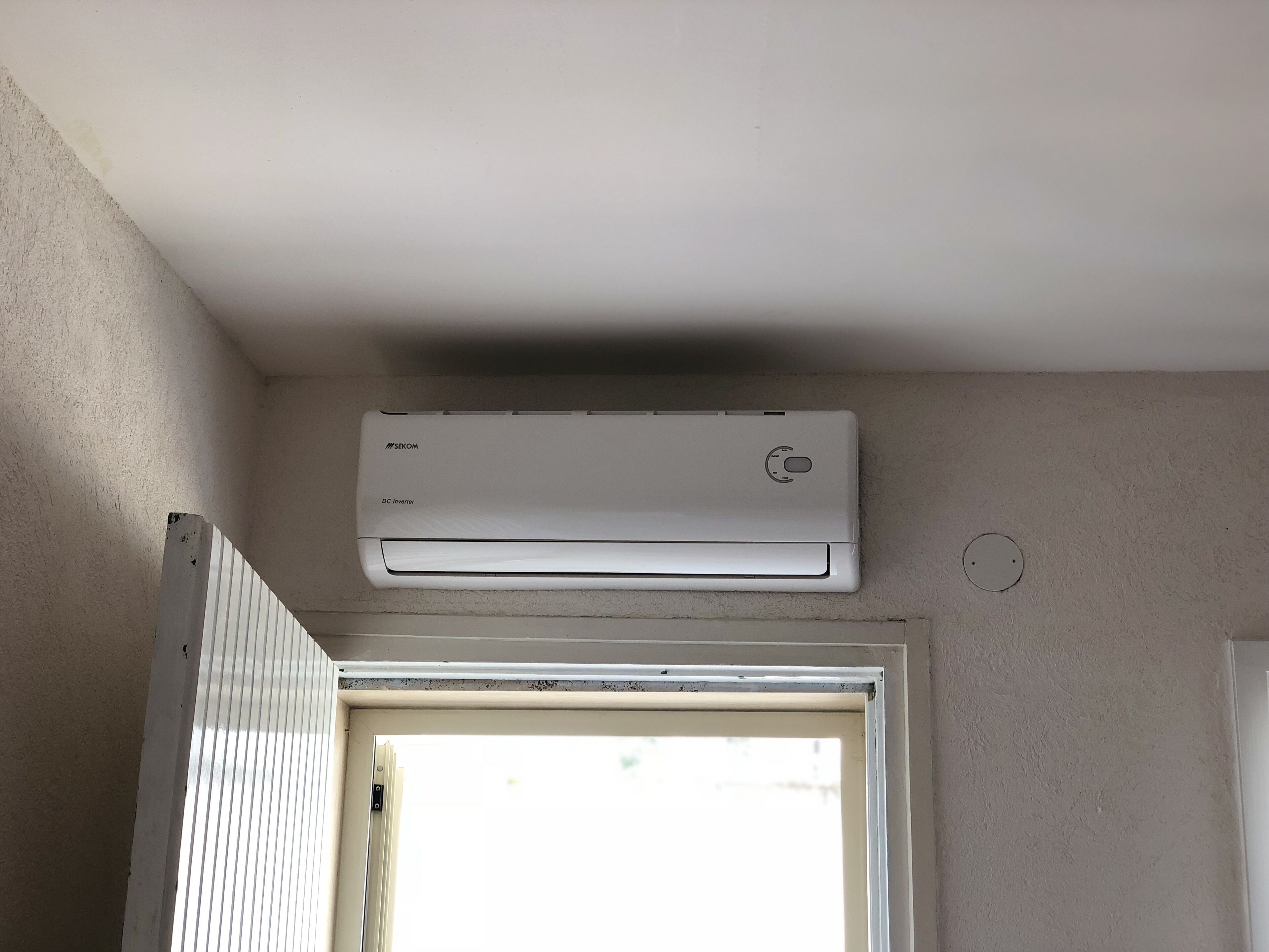 Een witte airconditioningunit bevestigd aan een muur boven een deur.