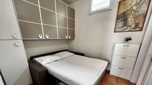 Un dormitorio compacto con una cama, una mesita de noche pequeña, un armario y un cuadro en la pared.