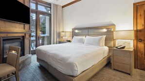 Habitación de hotel con una cama grande, cabecera de madera, mesita de noche con lámpara, una silla y chimenea.