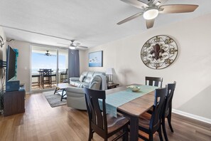 Una sala de estar moderna con comedor, ventilador de techo, ventana grande y vista al exterior.