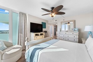 Un dormitorio con cama, televisor, cómoda, espejo y ventilador de techo.