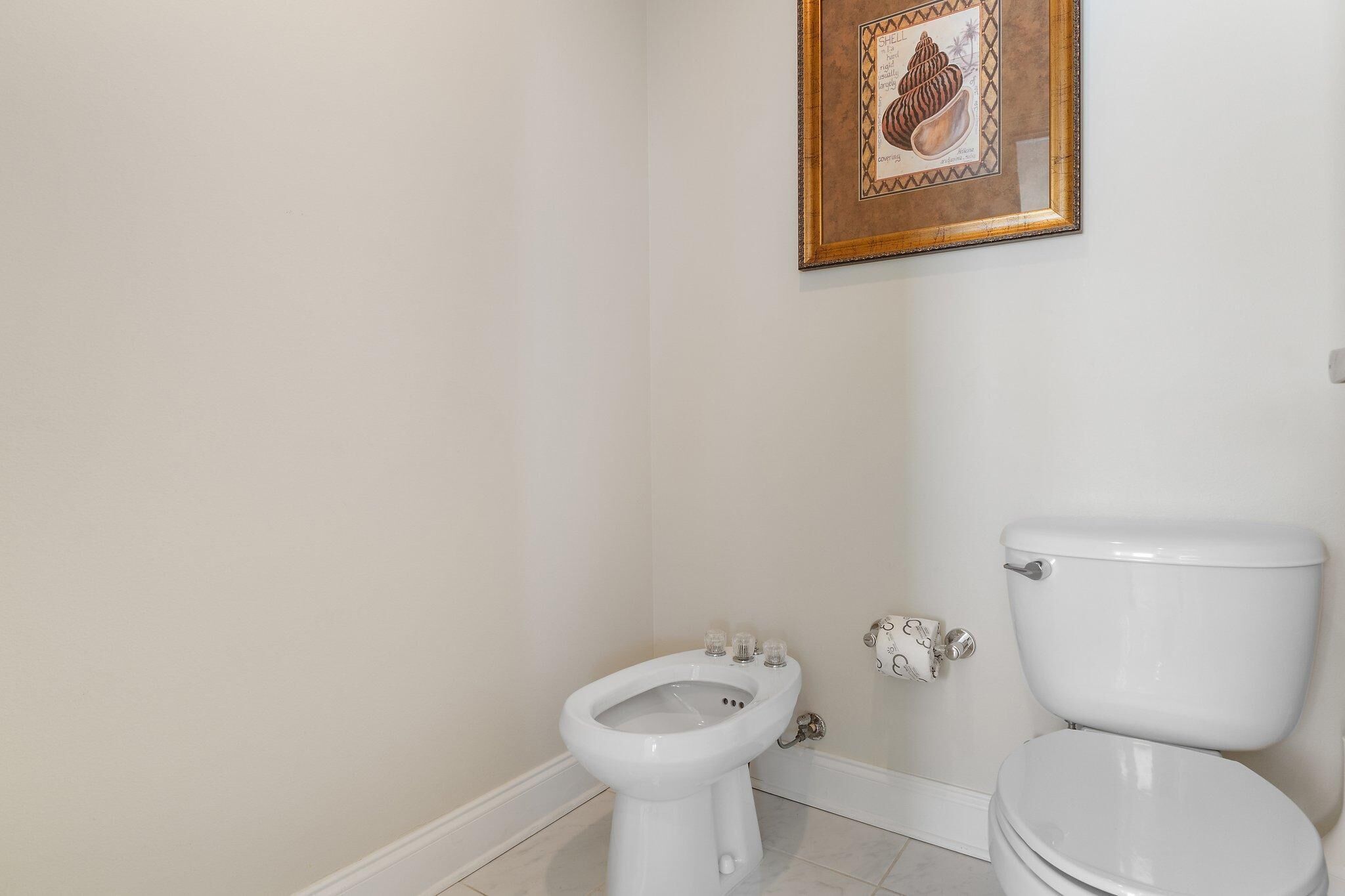 A bathroom with a toilet, bidet, and a framed picture on the wall.