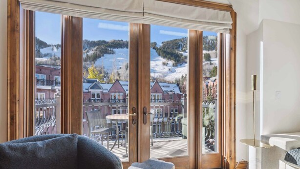 Une pièce dotée d’une grande porte-fenêtre coulissante qui donne sur un balcon offrant une vue sur un paysage enneigé et des bâtiments.