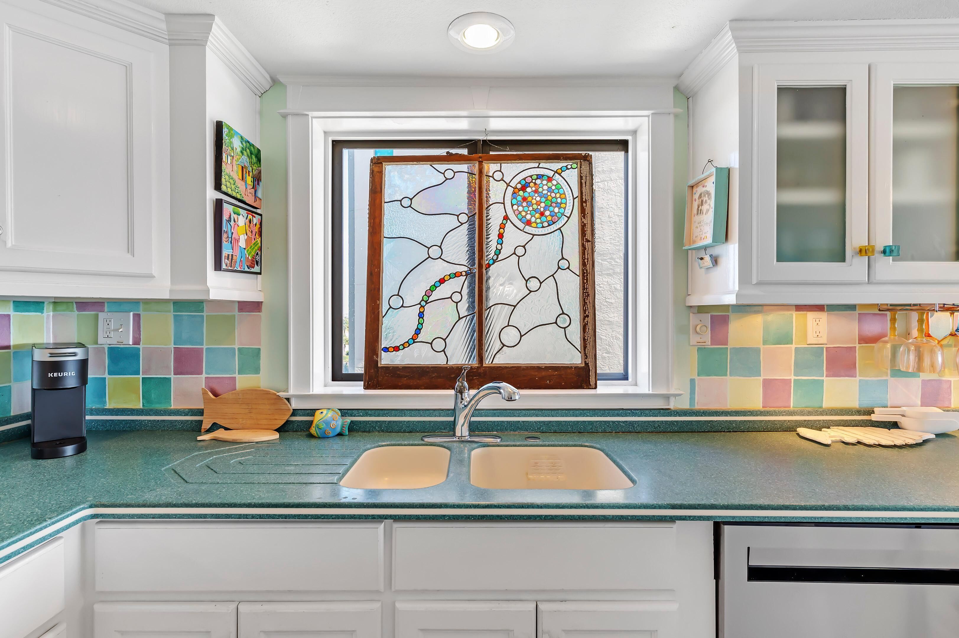 A kitchen with a double sink, a coffee maker, and a colorful backsplash.
