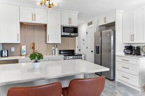 A modern kitchen with white cabinetry, stainless steel appliances, and a central island with seating. - 1 BR Top Floor Isle of Palms Oceanfront Condo | Pool | Free Wifi & Parking (Isle of Palms)