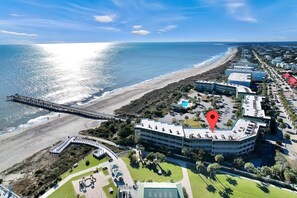 An aerial view of a coastal hotel with a beach, a pier, and a parking area.