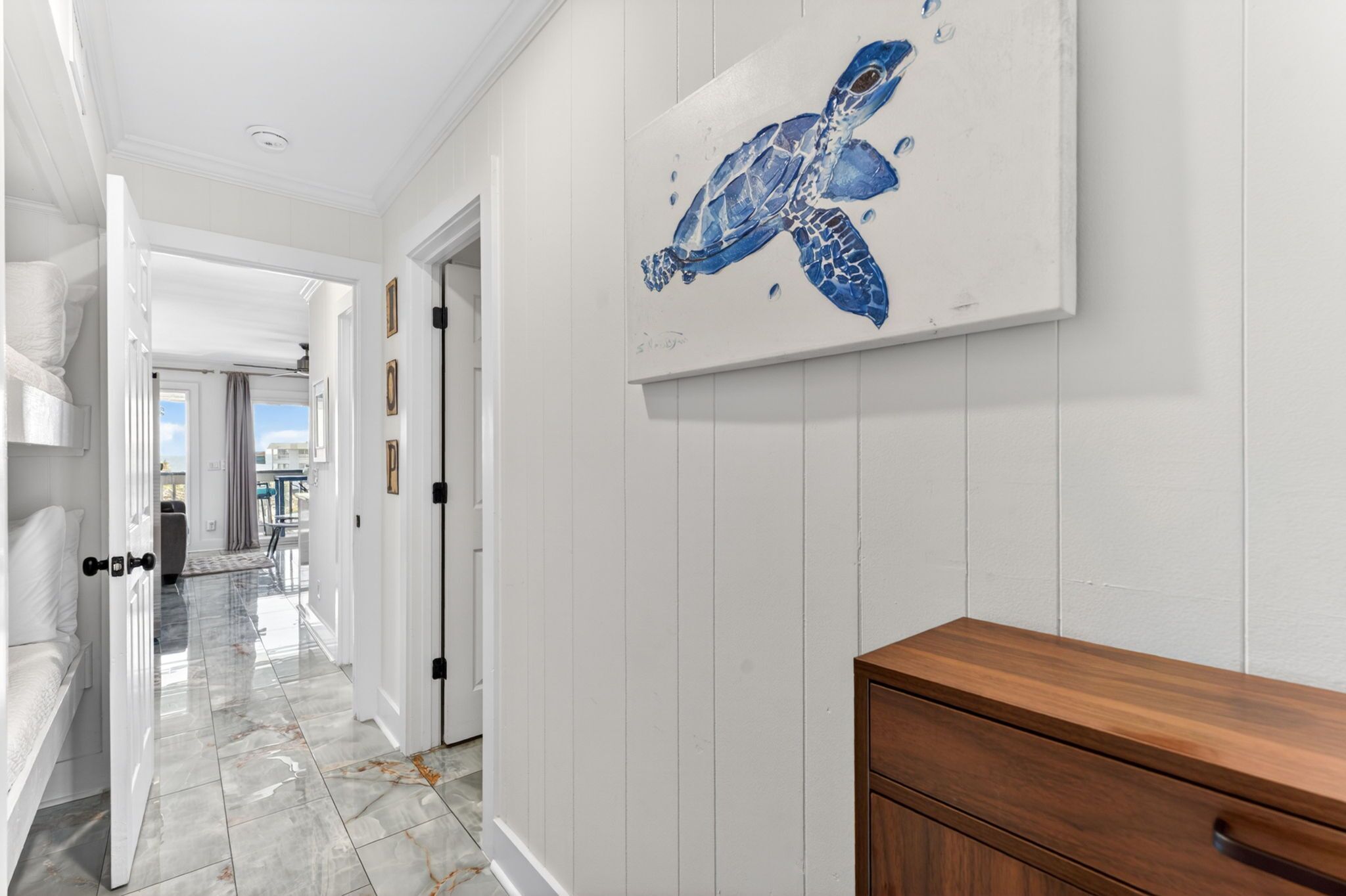 Un couloir avec une armoire en bois, une porte blanche et un tableau représentant une tortue de mer.