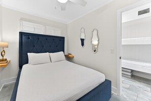 A bedroom with a large bed, a ceiling fan, a bedside table with a lamp, and a wardrobe.