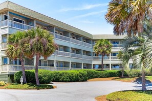 A multi-story hotel with balconies, palm trees, and a clear sky.