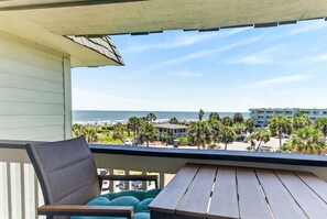 A balcony with a view of the beach, palm trees, and a building in the background.