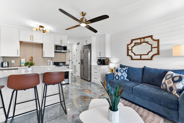 A modern kitchen with white cabinets, a bar area, a ceiling fan, and a blue sofa with patterned cushions.