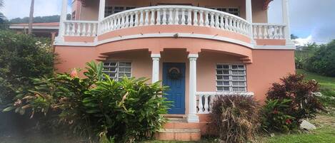 A two-story house with a balcony, a blue door, and a well-maintained lawn.