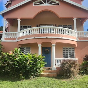 Une maison à deux étages avec un balcon, une porte bleue et un jardin à l’avant.