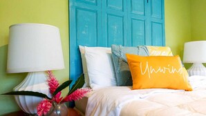 A bed with white bedding, a teal headboard, and decorative pillows including one with "Unwind" written on it.