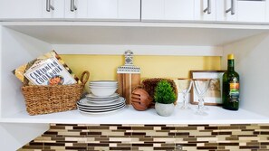 Una estantería de cocina con un libro de recetas caribeño, platos apilados, una botella decorativa, una planta pequeña y una botella de vino.