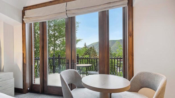 A hotel room with a large window, two chairs, a round table, and a wooden dresser. - The Aspen Mountain Residences 27A - Studio Residence (Aspen)