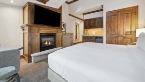 A hotel room with a fireplace, a bed, a TV, a desk, and wooden cabinets. - The Aspen Mountain Residences 27A - Studio Residence (Aspen)