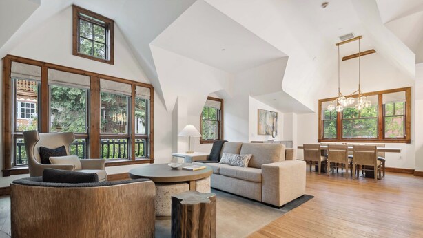 A spacious loft with high ceilings, large windows, and a cozy seating area with a round coffee table and cushioned chairs.
