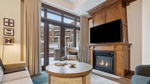 A living room with a fireplace, a television, and a large window with a view of buildings.