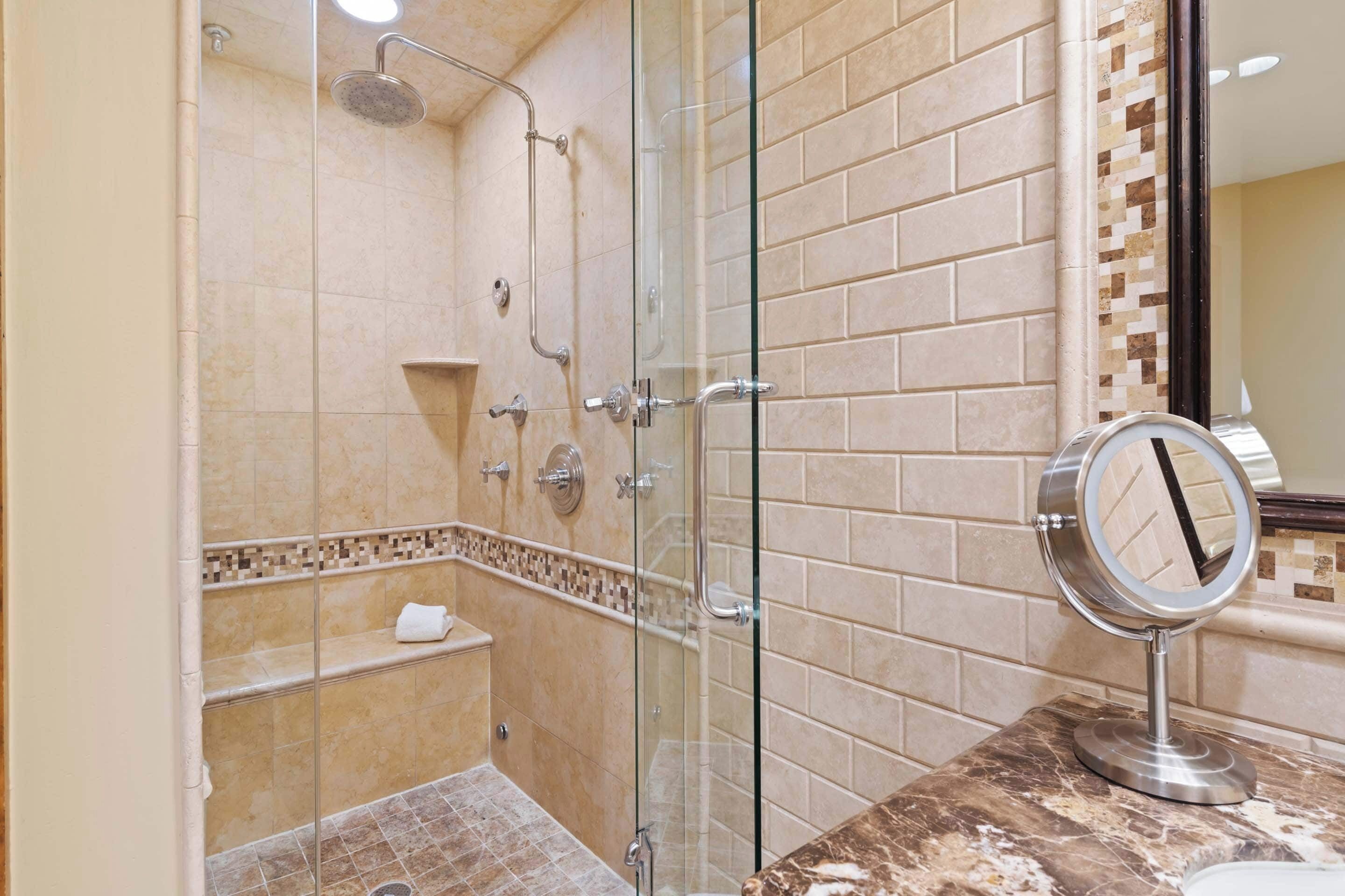 Un baño moderno con cabina de ducha de vidrio, encimera de mármol y espejo empotrado.