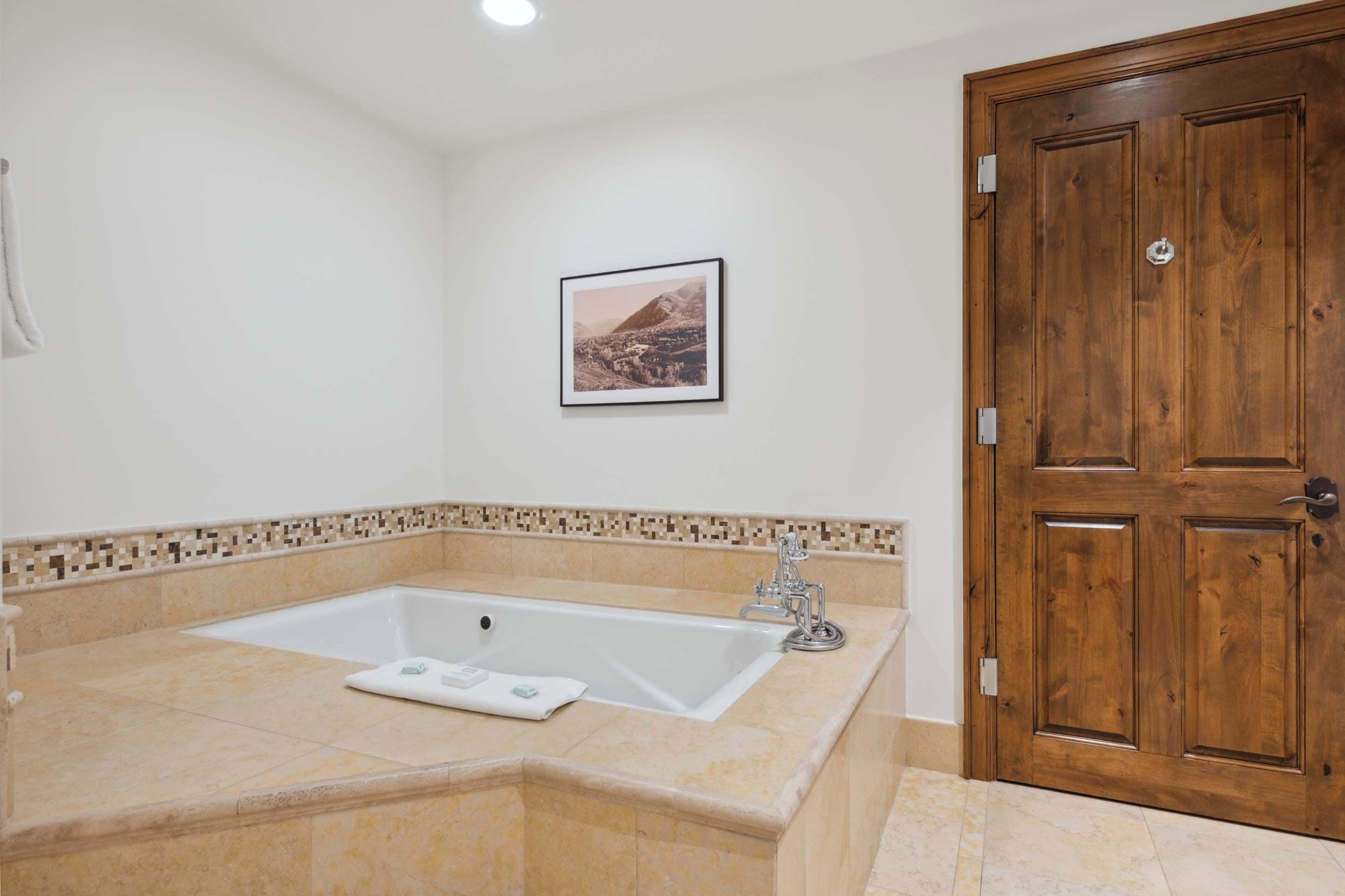 Une salle de bain avec une grande baignoire, une porte en bois et un tableau encadré au mur.