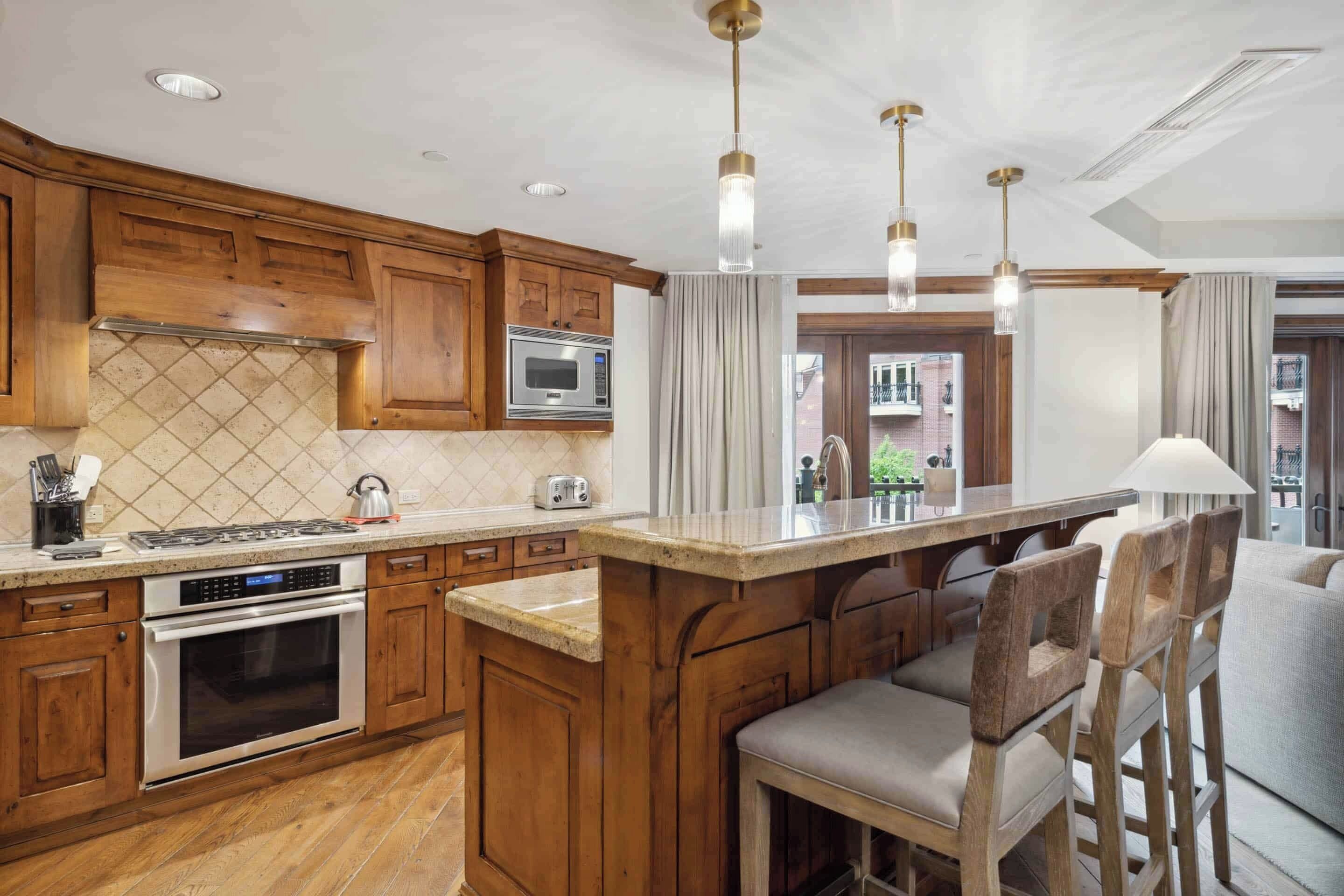 Una cocina con armarios de madera, un microondas integrado, una estufa a gas y una isla grande con taburetes de bar.